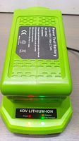 Green 40V lithium ion battery on charger showing power and charging indicator lights lit.