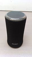 Front and top view of black cylindrical Bluetooth speaker with 'Soundcore' logo on mesh fabric, showing top control buttons and mesh texture.