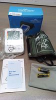Complete lot with digital blood pressure monitor, green cuff with printed instructions, batteries, user manual, and original blue box.