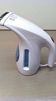Side view of the white handheld garment steamer showing blue transparent water reservoir and handle with red power button.