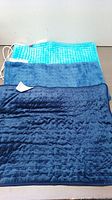 Three electric heating pads laid flat, showing a light blue/white textured pad and two dark blue quilted pads.