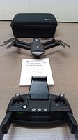Holy Stone HS260 drone with folded propellers, remote controller in front, instruction manual, and carrying case in background