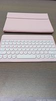 Pink Bluetooth keyboard with round white keys, detached from case, placed on wooden surface