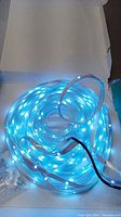 Coiled LED strip light glowing blue inside clear plastic casing on white background