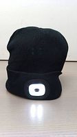 Black knit winter hat with a bright white LED light panel on the front cuff, illuminated to show the light function.