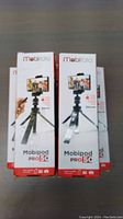 Five boxed Mobifoto Mobipod Pro50 tripods stacked vertically on flat surface.