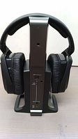 Front view of Sennheiser RS 175 Digital TV wireless headphones resting on their transmission and charging base, showing cushioned ear pads and control switches on base.