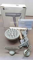 Hair dryer unit in gold with power cord and three attachments: diffuser, wide and narrow concentrator nozzles, shown with original box and manual.