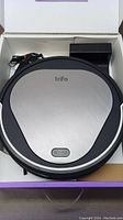 Trifo Emma Pet robot vacuum in open box with power button and home button visible on top, charging dock and power cord included.