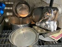 Photo showing multiple metallic cake pans including a deep tube pan, multi-tier round pans, muffin pan, and a large 3-D teddy bear pan stacked behind others.