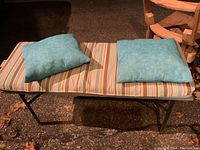 Outdoor metal bench with rectangular striped cushion and two smaller blue cushions