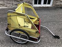 Side profile view of the yellow and red bike trailer with metal frame and fabric sides showing structure and wheels.