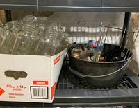 Box of assorted empty glass mason jars of various sizes, some with metal jar rings, against stove background.