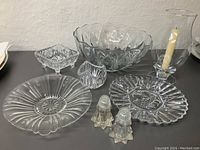Clear glass dining items arranged showing large bowl, candy dish, votive, salt and pepper shakers, and two serving plates
