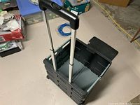 Side view of collapsible plastic rolling cart showing extendable metal handle and wheels.