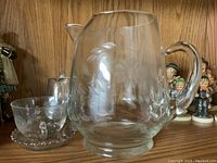 Large glass pitcher with etched cornflower pattern, seen close-up showing floral details and handle
