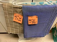 Two fabric pieces on hangers showing dimensions on orange sticky notes. Beige grid pattern and blue geometric pattern fabrics.