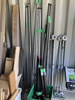 Tall galvanized pipes of varying lengths standing upright against a wall alongside wood planks, with pipe fittings including flanges attached to some pipes.