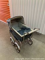 Front angle showing whole vintage doll buggy with canopy and fabric interior, metal wheels and handle.