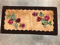 Full view of handmade hooked rug showing floral patterns and scalloped dark brown border.