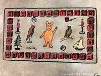 Full view of the rectangular handmade hooked rug depicting children's alphabet blocks, numbers, and colorful toys including a bear, parrot, owl, sailboat, ball, and toy soldiers on a beige background.