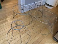 Four metal lamp shade frames arranged on wooden floor, showing top and side views