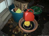 Photo of assorted flower pots stacked inside a large clay pot, gasoline container on top, and a blue plastic tub with a cardboard box inside.