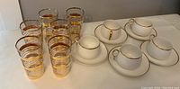 View of 6 gold trimmed drinking tumblers with 5 Nippon cups and saucers on a table
