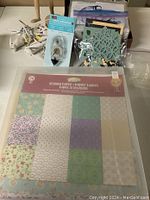 Photo of colorful patterned scrapbooking paper, plastic sleeves, glue guns, and crafting embellishments arranged on a table.