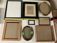 Various frames in different sizes and shapes laid flat on a table including black, gold, and wood-toned frames with glass and backing visible.