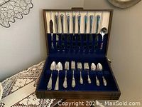 Full view of the silverware set arranged inside an open wooden case with blue felt lining.