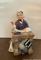 Front view of the Royal Doulton Schoolmarm figurine showing the elderly woman seated at her desk with inkwell and quill visible, and chalkboard hanging below the desk.