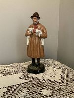 Front view of Royal Doulton Lambing Time figurine depicting an elderly man holding two white lambs, standing on a dark green base.