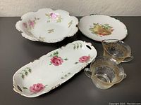 Porcelain serving dishes including scalloped bowl with rose floral decoration and round dish with fruit motif, and glass cream and sugar set with gold accents