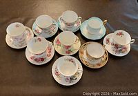 Top view of all nine tea cups with matching saucers arranged showing variety of floral patterns and gold accents