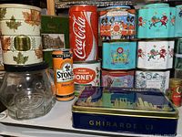 Overall view of vintage glass Kraft Peanut Butter jar, assorted collector tins including Coca-Cola, Fortnum & Mason Jubilee and Coronation tins, Stone's bitters can, and Ghirardelli tin.