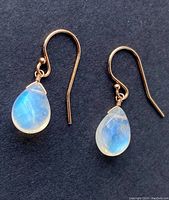 Pair of earrings on black background showing clear to rainbow blue iridescence of moonstone, gold hooks visible