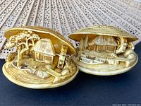 Pair of clam shell scenes featuring waterwheels and thatched roof houses, shown open revealing detailed interior scenes, made in Japan.