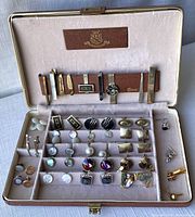 Full display of assorted cuff links, tie pins, and clips inside Shields accessory case, showing variety and arrangement.