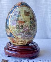 Whole view of the ceramic egg displayed on wooden stand with ruler showing approximate height of 5 inches.