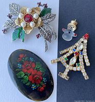 Photo of 3 holiday brooches and 1 Avon snowman charm laid flat on surface.