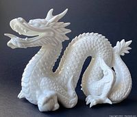 Front left angle view of white porcelain dragon figurine showing open mouth, detailed scales, and curled tail.