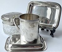 Photo of RCA sterling silver initial cup, pressed glass vanity jar with plated cover, and two Viking plate mini trays arranged together