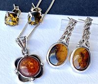 Close-up of amber stud earrings, pendant, and oval dangle earrings showing amber coloration and silver settings