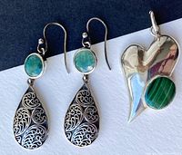 Photo showing pair of earrings with blue-green amazonite stones and teardrop filigree design next to silver heart-shaped pendant with green malachite stone.