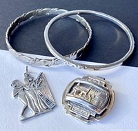 Photo showing two silver bangles with distinct carved and twisted designs along with two silver pendants: Peruvian design with shepherd and llama, and Egyptian musician pendant.