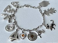 Full view of the sterling silver chain bracelet with 12 varied charms attached, laid flat on white background.