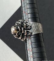 Side view of sterling silver ring showing floral pearl design and engraved bark texture on band with size scale