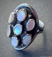 Front angled view showing six oval pearl inlays with iridescent white color and serrated bezels on oxidized silver ring face.