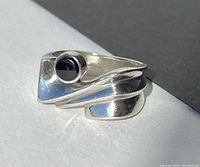 Close-up image of sterling silver ring with a round black stone on an offset modern design band.